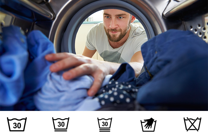 Wassymbolen wassen een man stopt blauwe kleding in wasmachine