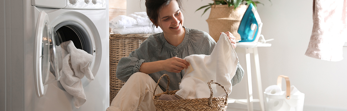 MONA Ratgeber Wäsche richtig trocknen Trockner Bild mit einer Frau vor einem Trockner mit frischen Handtüchern