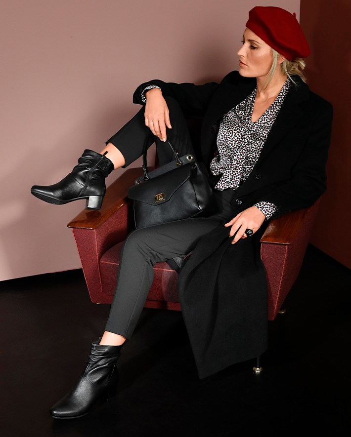 MONA Ratgeber Stiefel und Boots Intro Model auf einem Sessel mit Ledertasche und Stiefel
